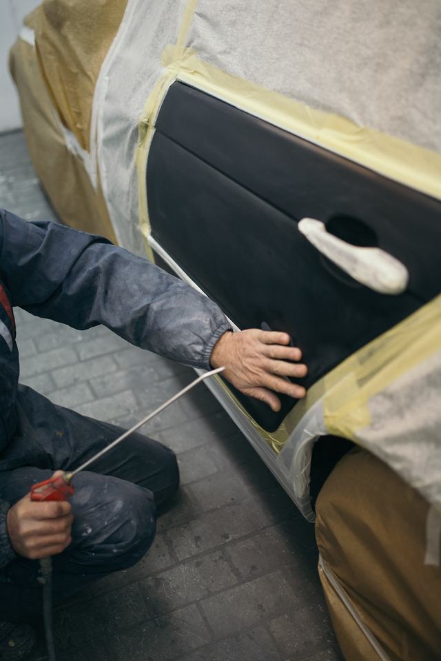 Een vakman blaast stof van een afgeplakt portier voor het bijwerken