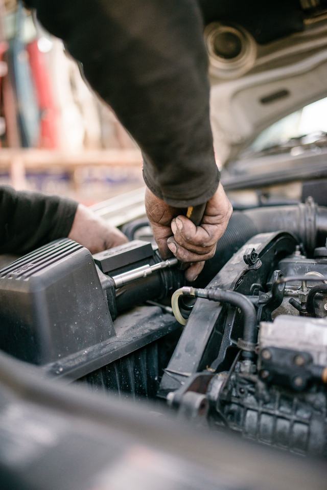 Een mecanicien werkt met een sleutel aan de motor van een wagen met open motorkap