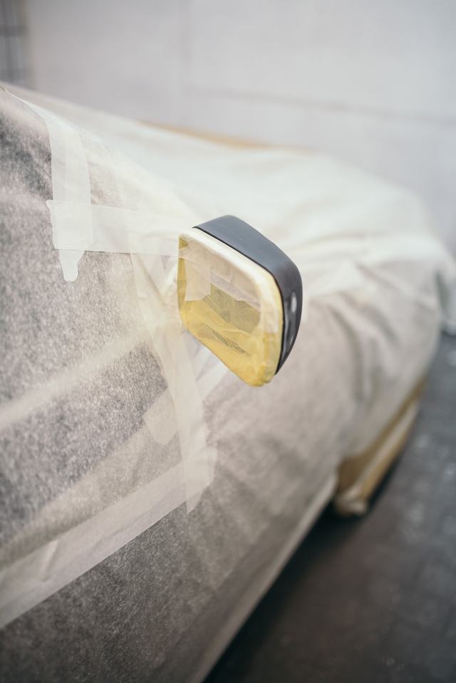 Een buitenspiegel ingepakt in folie en tape, de rest van de wagen afgedekt