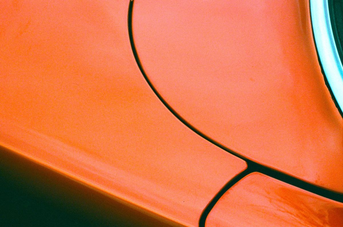 Close-up van een oranje gelakte wagen, het licht glijdt over de ronding van het spatbord